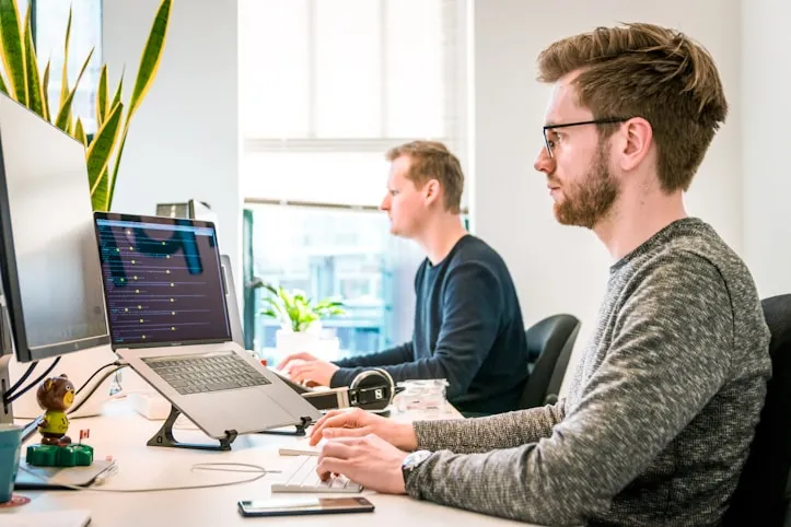 A white man in a sweater is working at the computer providing training and support for Camtasia